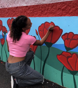DeeBee Whimzy painting flowers on a mural wall.
